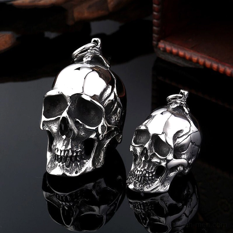 Twin skull pendants with detailed bone carving reflected on black surface with wooden aesthetic