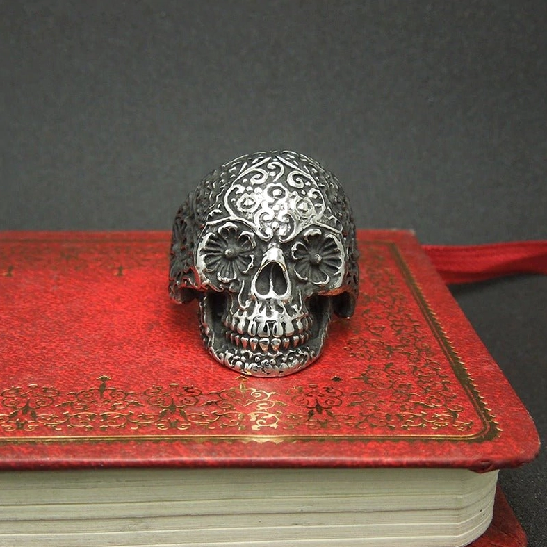 Ornate floral engraved skull ring displayed on vintage red book, antique dark silver stainless steel finish