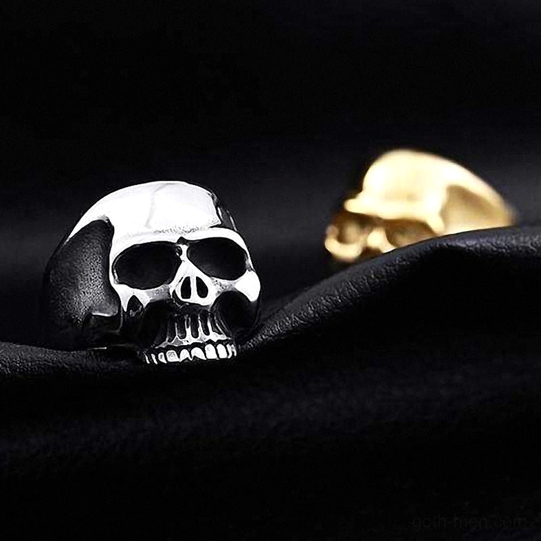 Silver and gold finished skull rings oblique side view on dark fabric background, demonstrating compact gothic ring style and metal finishes