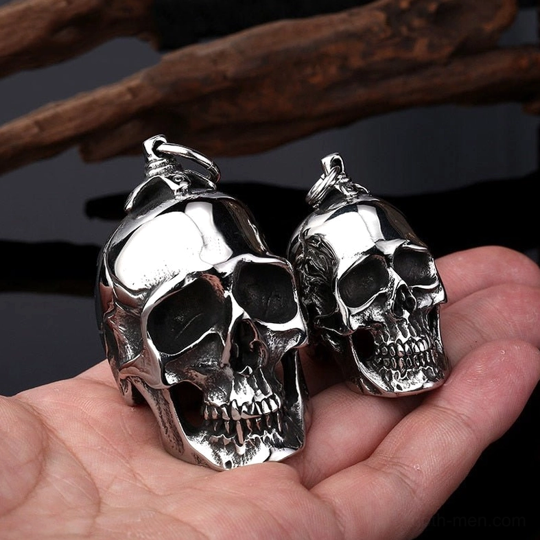 Dual skull pendants in hand on dark background showing polished silver finish and scale
