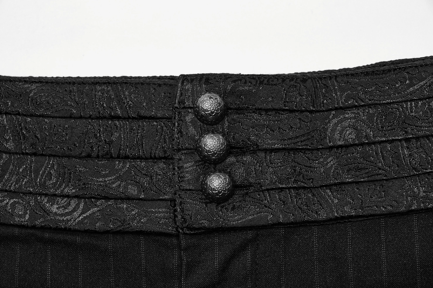 Top-down close-up of black striped pants waist closure, embossed decorative fabric pattern, button hardware