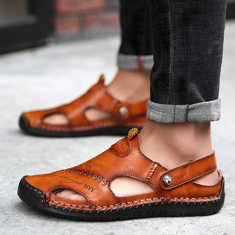 Man in rolled-up jeans wearing tan leather gothic sandals with closed toe design on outdoor street